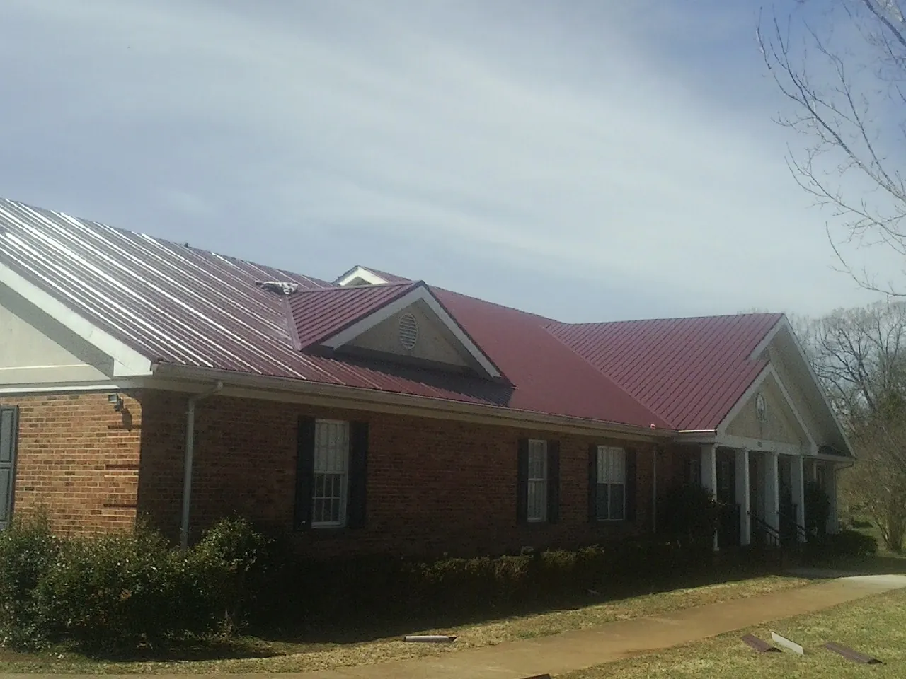 Red metal roof with gabled entries on a long brick building, from a Hail Damage Roof Repair job in King George