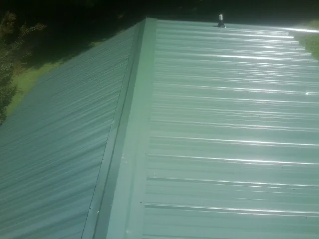New green metal panels meeting at the ridge of a roof — Flat Roof Repair work by our crew in King George