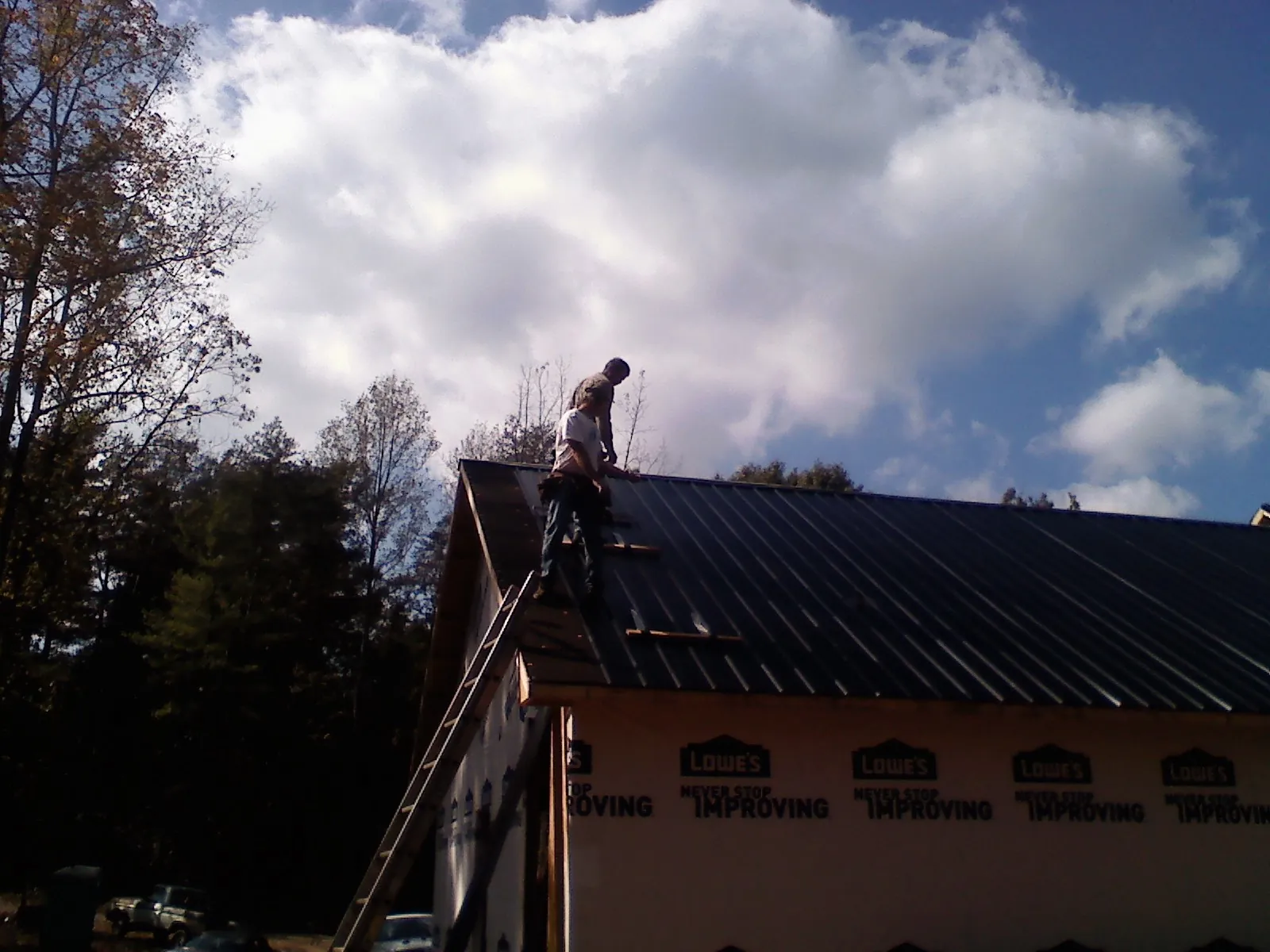 Roofer fastening dark metal panels high against a cloudy sky, from a Roof Inspection job in King George