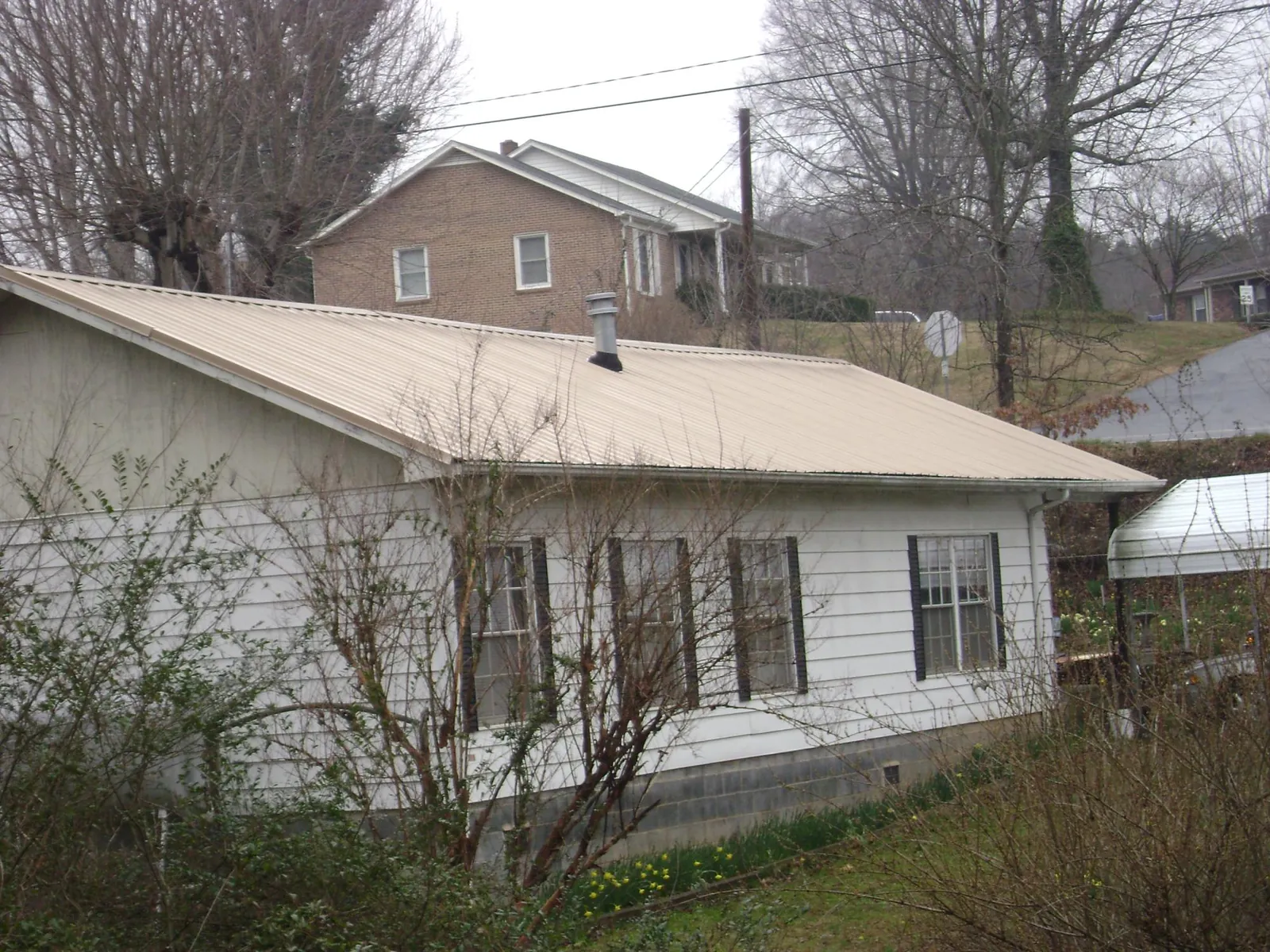 Tan metal roof on a white sided house set into a hillside — Commercial Roofing by Roofing Brothers in King George